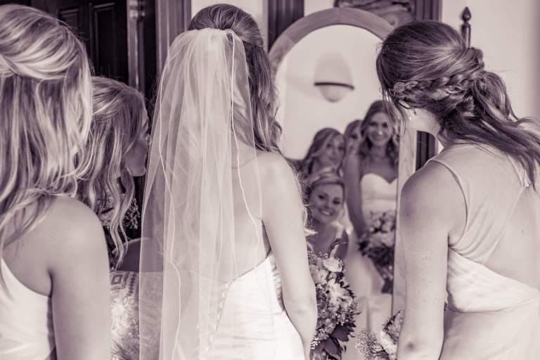 Wedding Photos. LIFELIGHTLENS image of bridesmaids gathered around bride and mirror.
