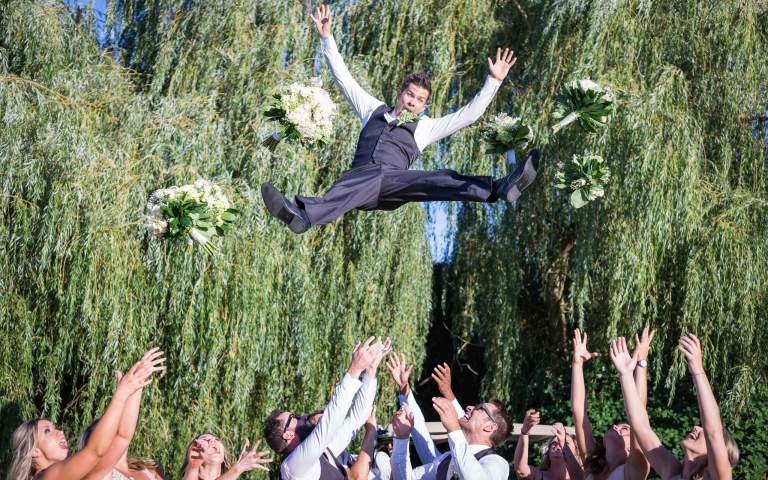 Wedding Photos. LIFELIGHTLENS image of a groom being tossed high into the air.