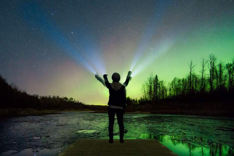An image of a person search the night skies for northern lights, using a flashlight